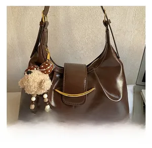 Detail of dark brown glossy leather underarm bag with gold crescent hardware and bear charm