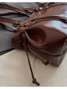 Detailed view of dark brown glossy leather shoulder bag with side drawstring accents