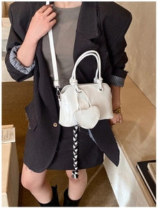 Close-up of white patent leather handbag featuring heart charm and woven fringe detail