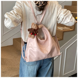 Pink faux leather tote bag with teddy bear charm shown worn by a model on stairs