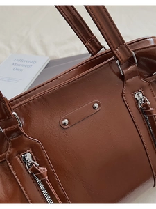 Detailed close-up of brown leather Boston bag showing metallic zippers and textured finish