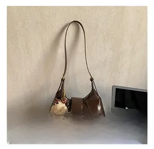 Detail of dark brown leather crescent bag with gold metal buckle and cute bear charm