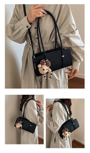 Detail of black pebbled leather baguette bag featuring a plush bear and pearl charm
