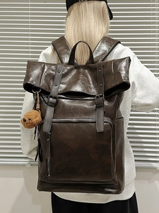 Retro deep brown leather backpack with roll-top design and plush bear charm on model