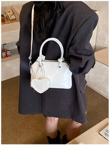 Detail of white glossy shell bag with heart charm and knot handle on a model