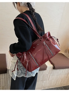 Detail of dark red glossy shoulder bag with multiple zippers and long leather tassels