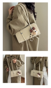 Detail of cream rectangular shoulder bag with teddy bear charm and sleek twin straps