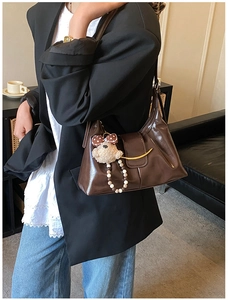 Detailed shot of dark brown leather underarm bag with gold crescent clasp and bear charm