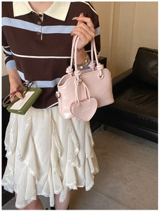 Detail of pink faux leather handbag with knot handle and heart charm on lace dress
