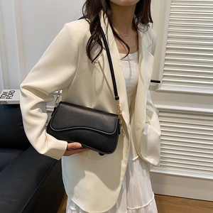 Borsa sottobraccio in pelle nera con patta indossata da una modella in abito bianco