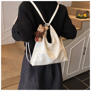 Detailed view of white faux leather hobo bag with a cute bear plush charm on a black sweater