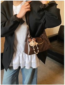 Detail of dark brown glossy underarm bag with golden arc trim and plush bear charm