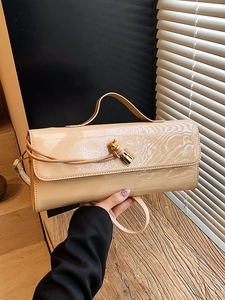 Sac à main élégant en cuir verni nude avec fermoir nœud doré sur surface en bois