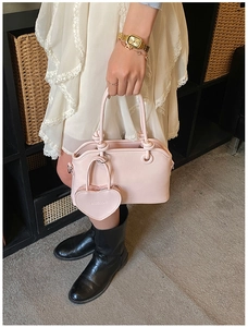 Detail view of pink leather handbag with heart charm and brand embossing in a lifestyle setting
