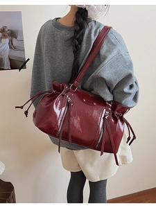 Detail view of burgundy oiled leather shoulder bag with tassels and drawstring on model