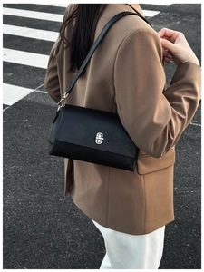 Detail of a black matte leather crossbody bag with silver buckle worn by a model in a suit