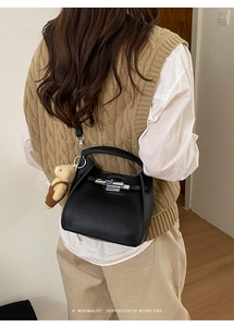 Detail of black lychee grain leather bucket bag with silver turn-lock and bear charm