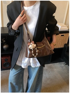 Detail of a dark brown leather shoulder bag with gold hardware and a cute plush charm
