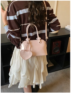 Detail of pink faux leather handbag with embossed heart pendant and dual handles