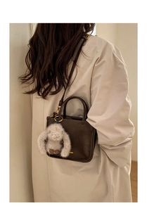 Detail of dark brown leather bucket bag with plush rabbit charm on a beige trench coat