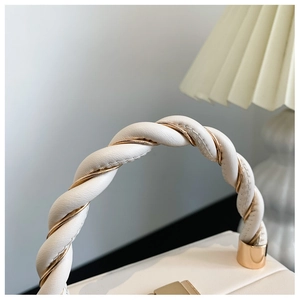 Detail of twisted white leather and gold metal handle on a structured handbag