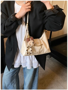 Detail of cream hobo shoulder bag with gold hardware buckle and plush bear charm