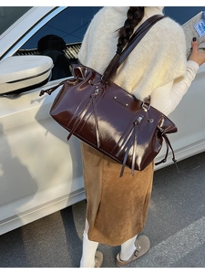 Detail of dark brown glossy leather Boston bag with metallic zippers and long fringe tassels