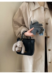Détail du charm lapin en peluche gris sur un sac seau noir avec des gants en tricot