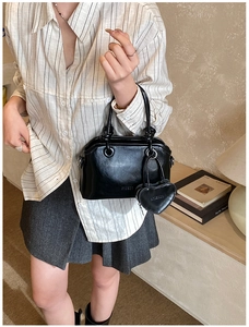 Close-up of black glossy leather handbag with heart-shaped charm in a cozy indoor setting
