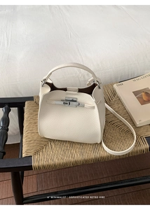 Close-up of off-white lychee texture bucket bag with silver metal clasp on woven stool