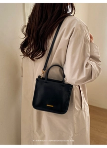 Détail d'un sac seau en cuir noir avec logo en métal doré et bandoulière réglable
