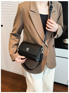 Detail of minimalist black leather crossbody bag with silver twist lock and adjustable strap