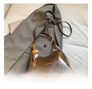 Détail du sac hobo en cuir brillant marron foncé avec pompon et perles en bois