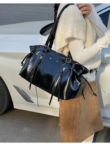 Street style shot of a black glossy shoulder bag with silver hardware and tassel zippers
