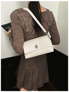 Detail of minimalist beige PU leather crossbody bag with silver rotating lock on model