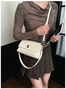Detail of a creamy white minimalist crossbody bag with adjustable strap and metal clasp