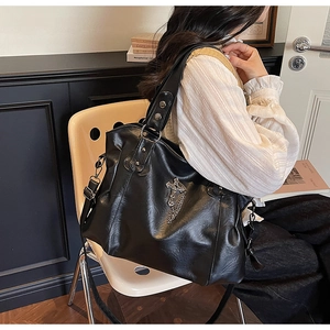 Detail view of black tote bag with silver cross charm and chain on adjustable strap