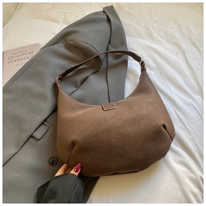Dettaglio della borsa a mezzaluna in camoscio marrone con texture opaca su tessuto bianco