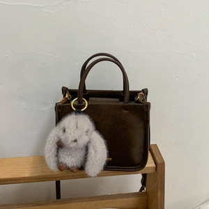 Détail du sac seau vintage marron foncé avec un lapin en peluche gris et des boucles dorées