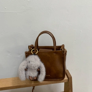 Détail d'un sac seau vintage en cuir marron avec un charme de lapin en peluche et métal doré