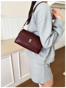 Close-up of wine red leather handbag featuring a silver twist lock on a gray suit model