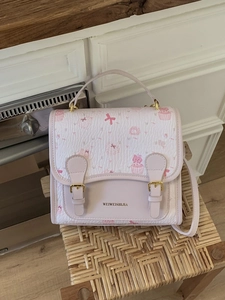 Cute pink cartoon cat print handbag with double buckle straps on a wooden stool