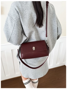 Deep red crossbody square bag with silver turn-lock clasp shown on a model's shoulder