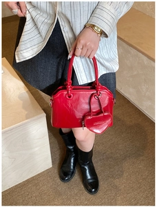 Detail of red glossy handbag with heart charm and brand logo held by a model