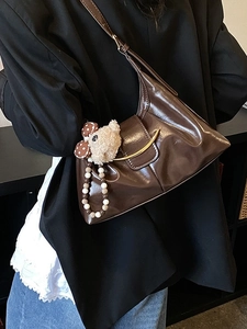 Glossy brown retro shoulder bag with golden hardware and plush charm on black blazer