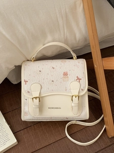 Cute cream-white tote bag with cartoon cat prints and adjustable buckles on bed