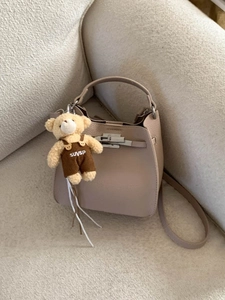 Chic beige litchi pattern bucket bag with cute bear charm on a soft boucle sofa