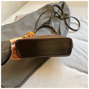 Detail of deep brown glossy leather bag with gold hardware and amber bead charm
