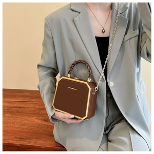 Detail of coffee brown suitcase crossbody bag with golden frame and twisted handle