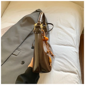 Detail of dark brown leather underarm bag featuring decorative wooden bead tassel and gold hardware